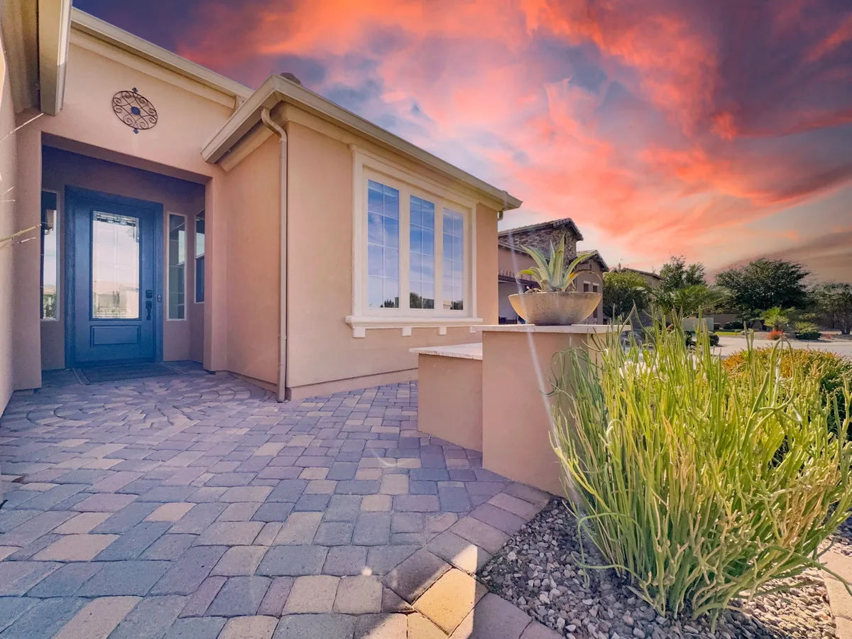 A charming home exterior featuring a bold blue door, expansive windows, thoughtfully maintained garden beds, and a paved path leading toward the entrance. The landscaping and inviting pathway hint at neighborly interactions and the enjoyment of outdoor spaces.