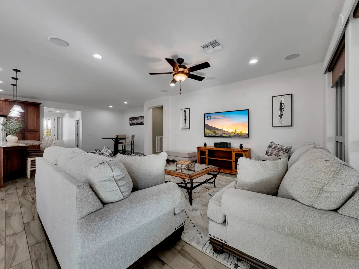 A welcoming living room featuring comfortable sofas arranged around a wooden coffee table, a television displaying a scenic image, and decorative artwork on the walls. Soft natural light filters in, enhancing the cozy and relaxed mood of the space.