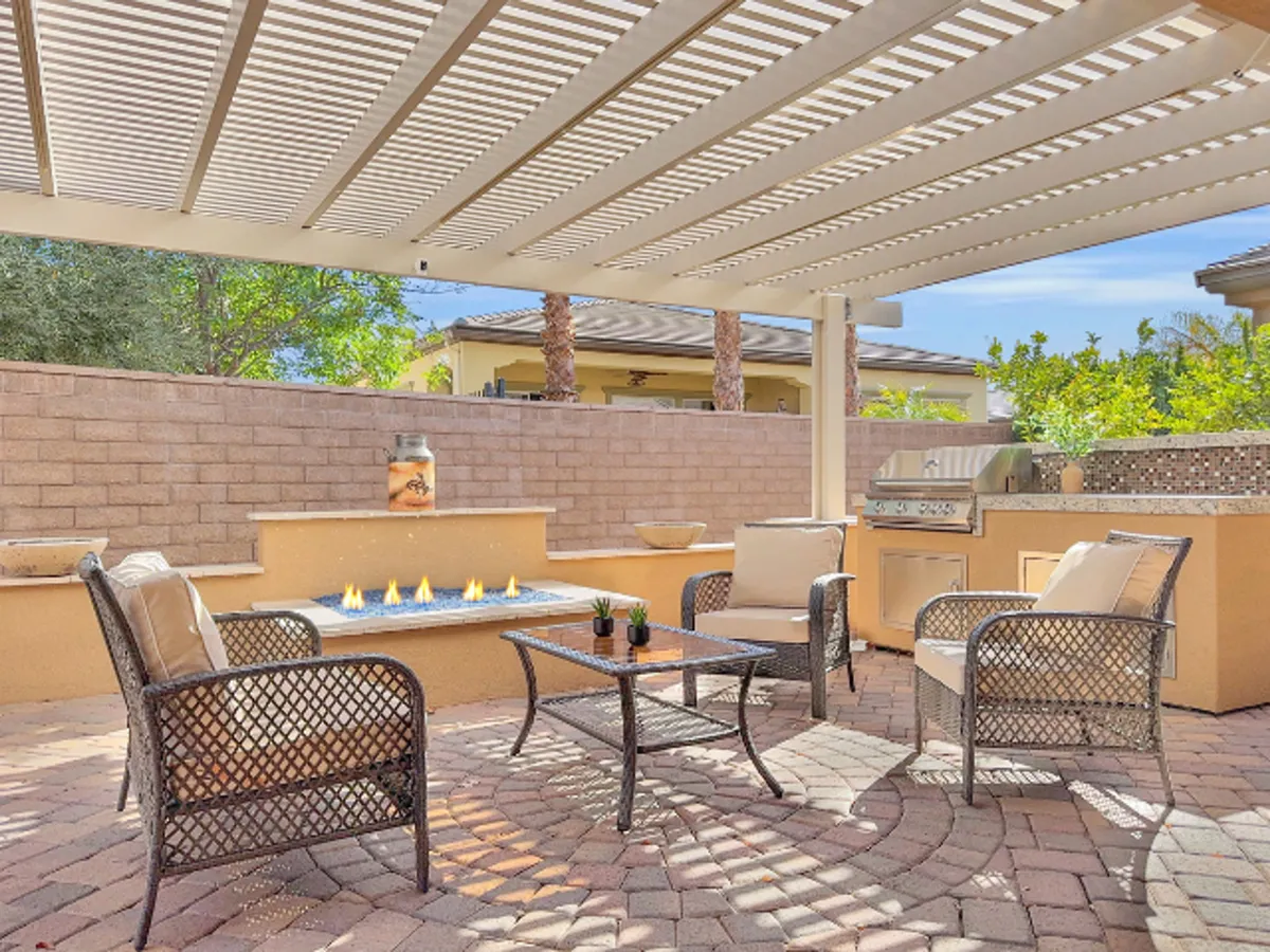 An outdoor living area featuring a cozy fire feature, ample seating, a grill, and lush landscaped greenery. The space is welcoming and designed for social gatherings, relaxation, and entertaining guests, with an inviting ambiance ideal for sunset evenings or lazy afternoons.