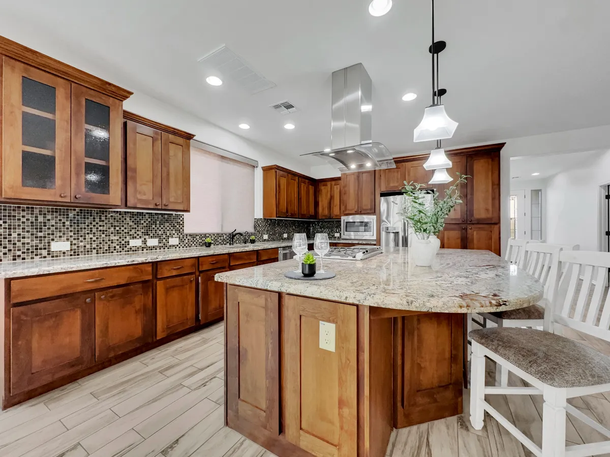 A stylish kitchen with a prominent island, granite countertops, warm wooden cabinetry, and stainless steel appliances. The space looks ready for both everyday meals and festive gatherings, with a layout that invites participation.