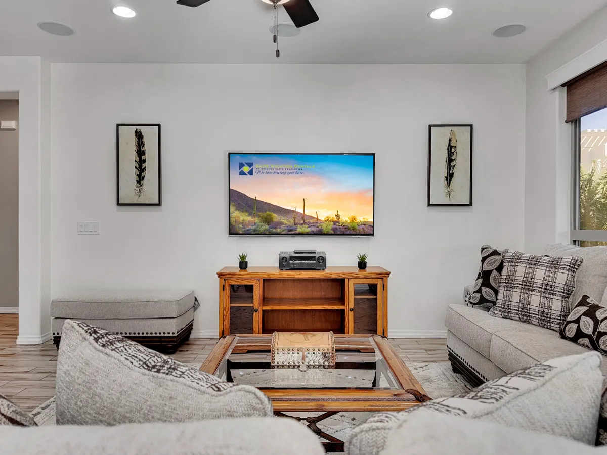 A cozy interior scene with plush couches, a TV featuring a scenic display, a wooden console table, and tasteful decorative artwork. The space is bathed in warm light, creating an inviting environment ideal for unwinding or entertaining.