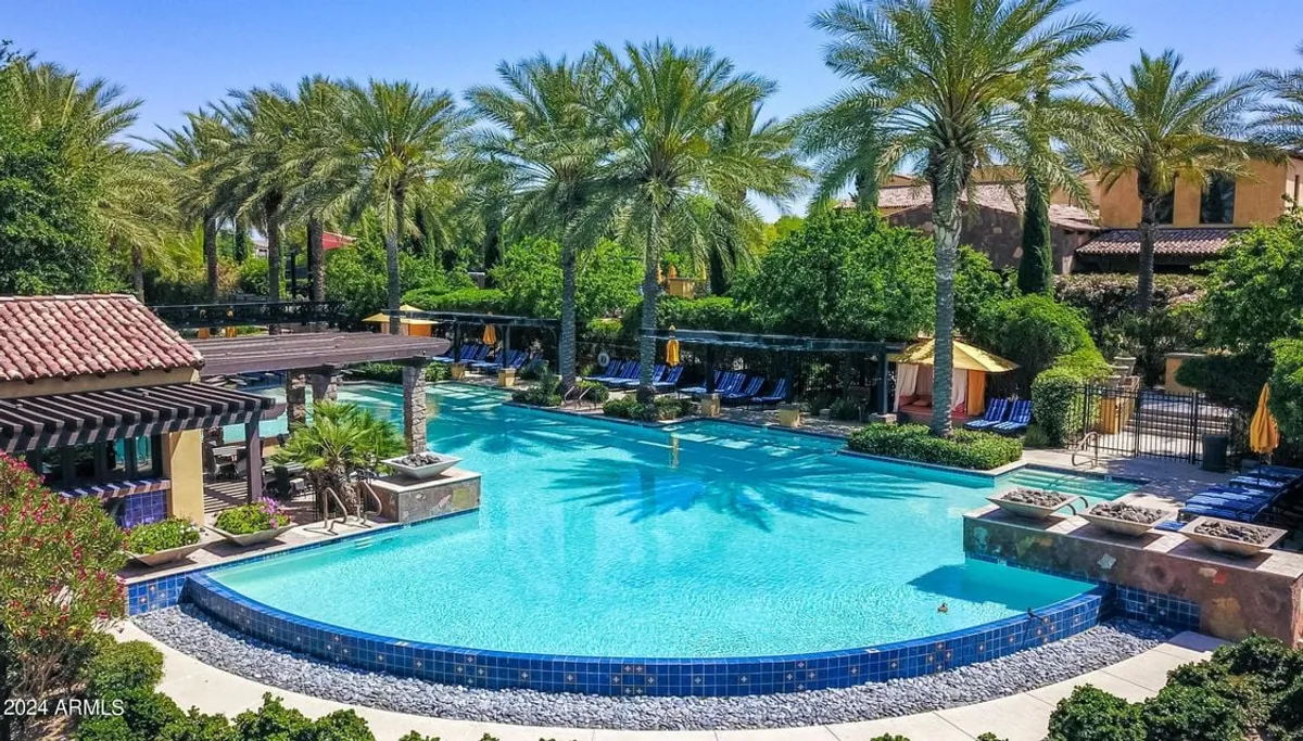 The scene features a luxurious swimming pool surrounded by palm trees, plush lounge chairs, and stylish cabanas. The tranquil setting is enhanced by elegant poolside landscaping, inviting residents to relax, sunbathe, or socialize by the water.