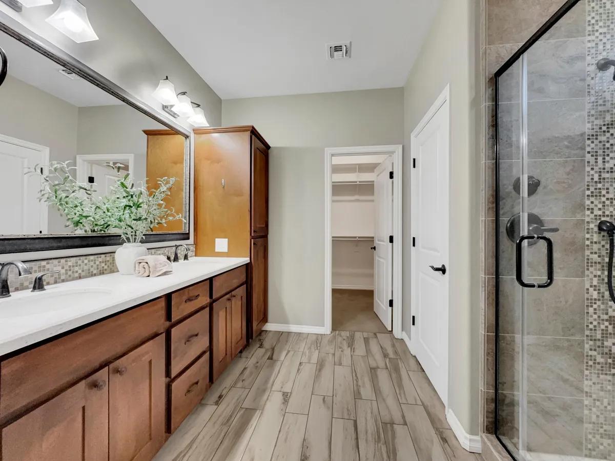 A spa-inspired ensuite bathroom with a double sink vanity, glass shower enclosure, large mirror, and wood cabinetry. The tranquil, organized setting invites relaxation and rejuvenation, perfect for unwinding after an active day.