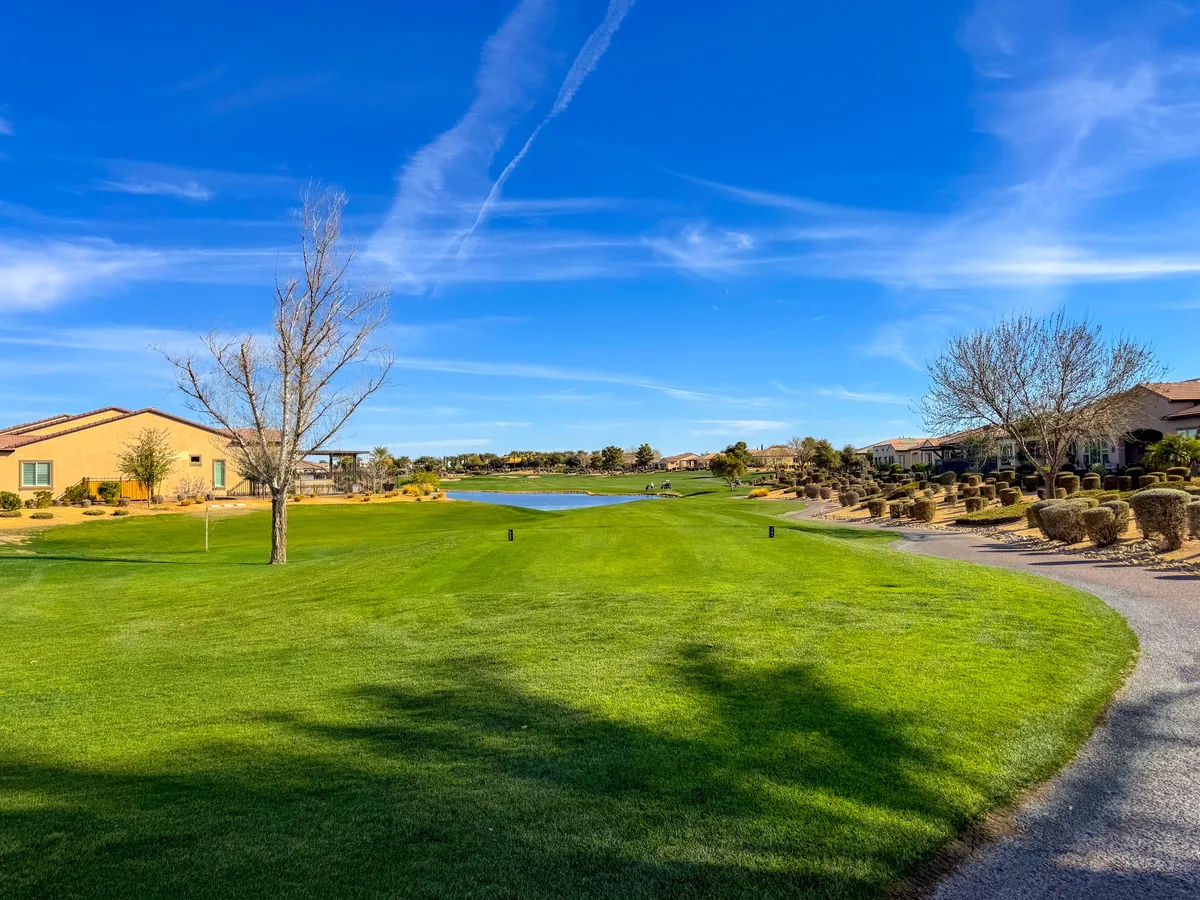 A breathtaking exterior view of the community with a lush green lawn, a peaceful lake, and scenic homes set against the backdrop of a golf course. The scene radiates serenity and captures the essence of outdoor leisure activities like walking, golfing, or simply relaxing by the water.