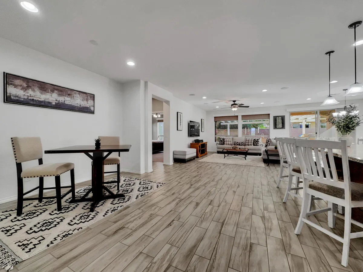 This image presents a dining table with chairs adjacent to a living area and a kitchen island with bar stools. The arrangement is open and airy, fostering easy movement and casual, social dining experiences, with natural light enhancing the scene.