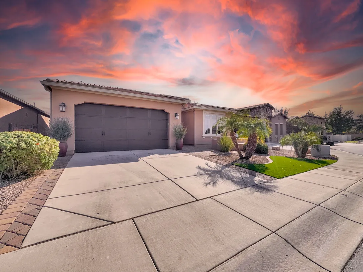 A wide driveway fronts a modern garage door, accented by well-kept landscaping and a backdrop of open sky. The open space suggests gatherings, outdoor relaxation, and a gateway to local adventures just beyond the home.