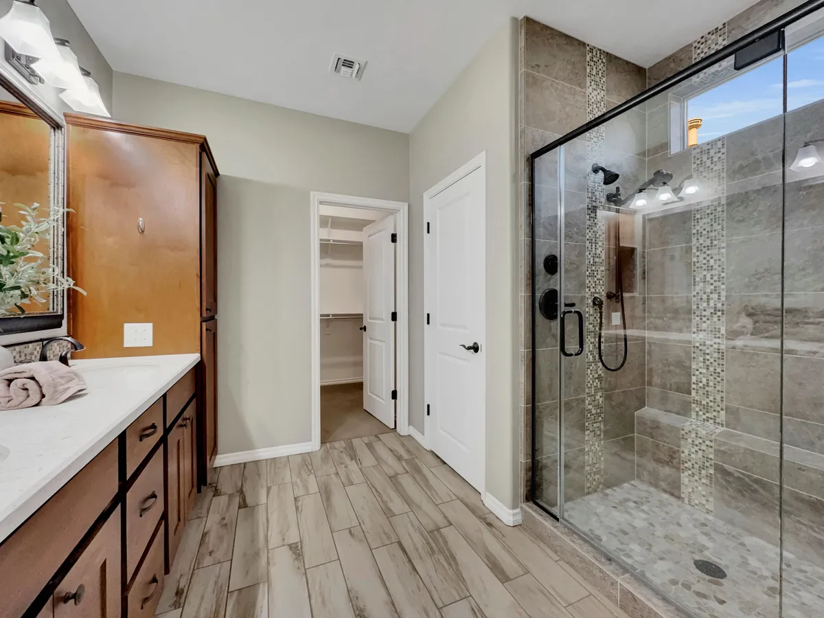 A bright, spa-inspired bathroom features a glass shower enclosure, double sink vanity, and wood cabinetry. Soft morning light streams through the window, creating an atmosphere of serenity and self-care.