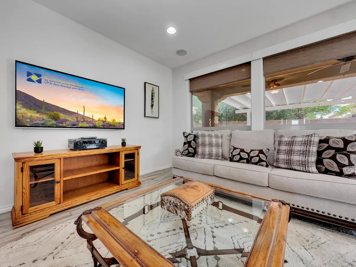 A bright, comfortable living room featuring a sofa, coffee table, TV with a landscape image, and a wooden cabinet. Large windows allow abundant natural light, and the space feels open and welcoming, ideal for enjoying the view or hosting guests.